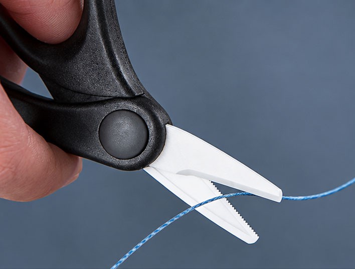 Close-up of ceramic fishing scissors cutting braided PE line with a single-sided serrated blade